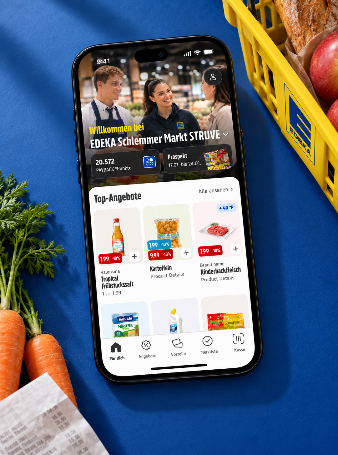 EDEKA grocery app on an iPhone against a blue backdrop beside a yellow shopping basket and fresh groceries
