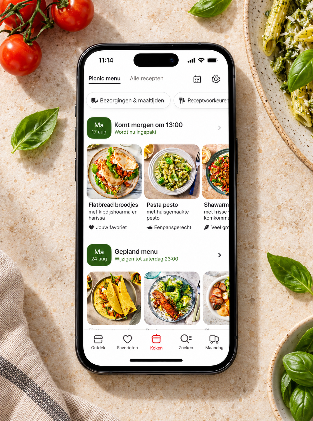 Picnic Menu meal planning app on a phone surrounded by pasta, basil and tomatoes